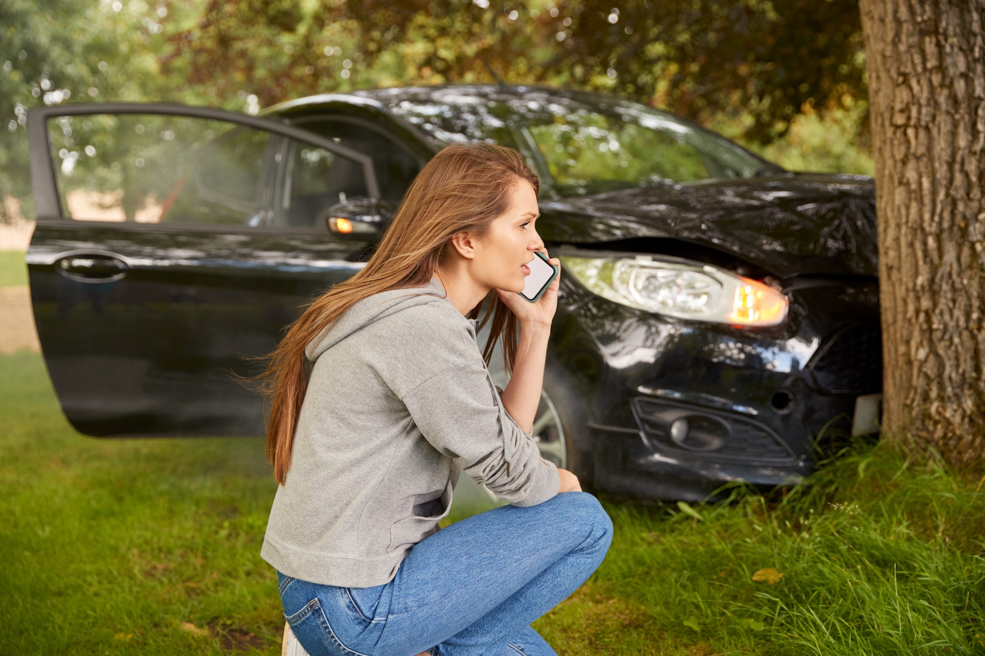 Woman Next To Car Crashed Into Tree Inspecting Accident Damage And Calling Emergency Services