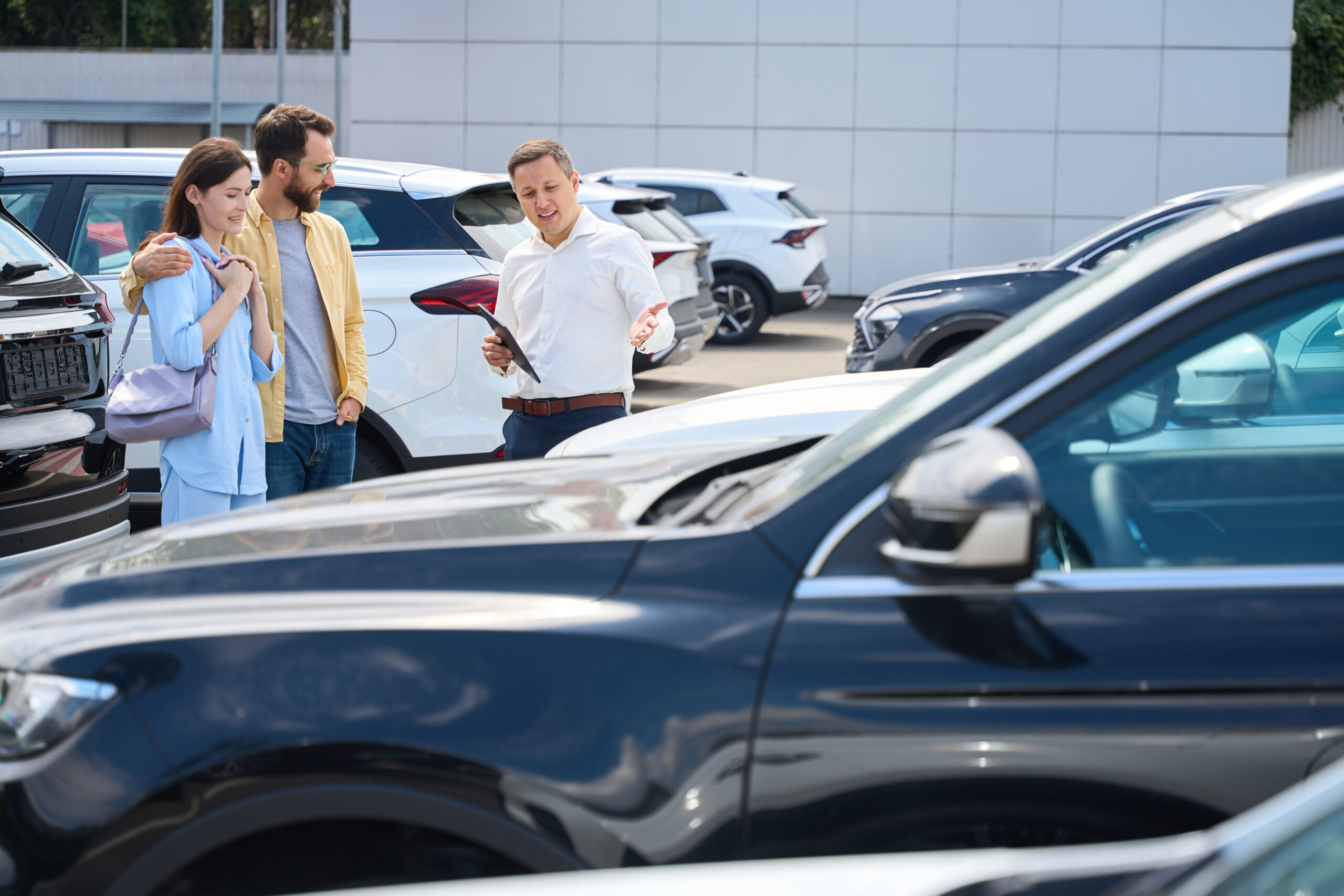 Buyers choose a car in the yard of a car dealership, a consultant helps them