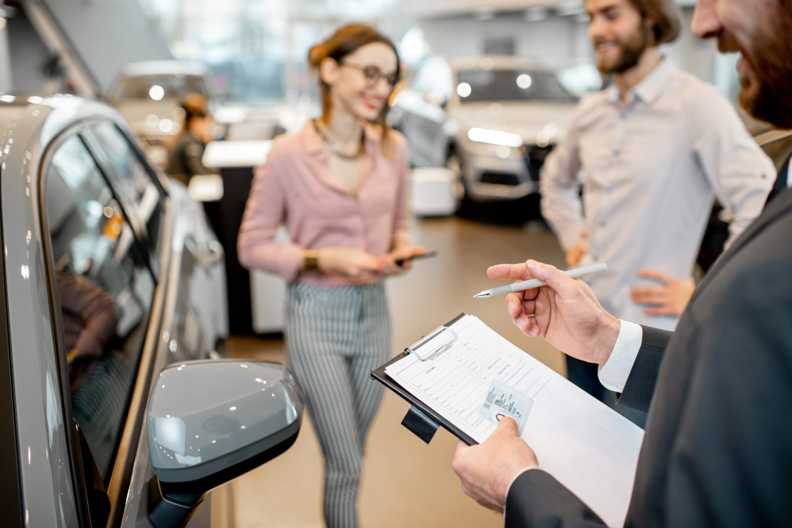 Manager filling test drive documents standing with young couple clients in the showroom